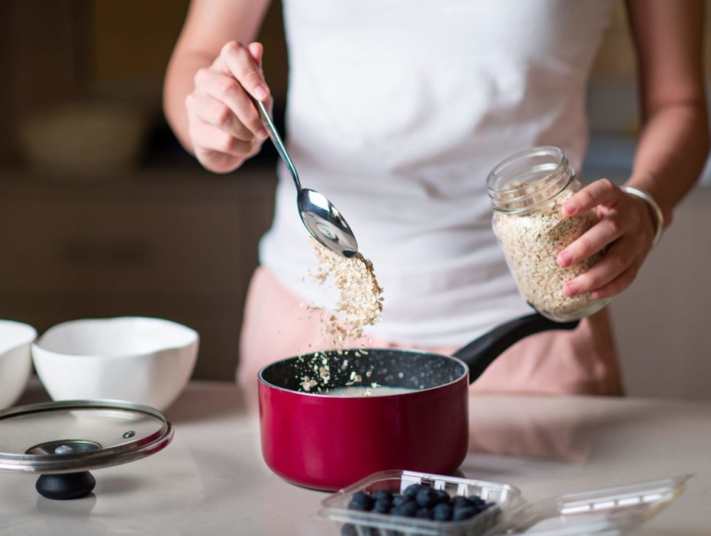 Femme préparant des céréales d'avoine pour le petit-déjeuner du matin et ajoutant des ingrédients dans la cuisine à la maison. Préparation d'un repas biologique sain, riche en fibres et en nutriments.